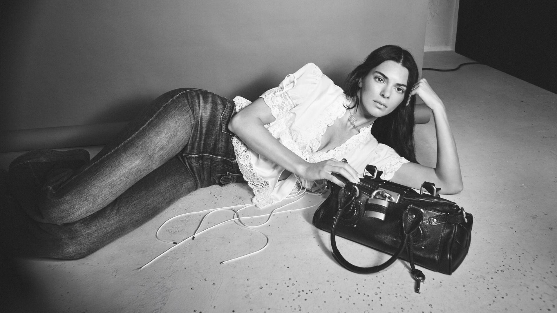 Black-and-white 4K Ultra HD PC desktop wallpaper of a woman reclining on the floor in jeans and a ruffled blouse, propped on one elbow beside a leather handbag.