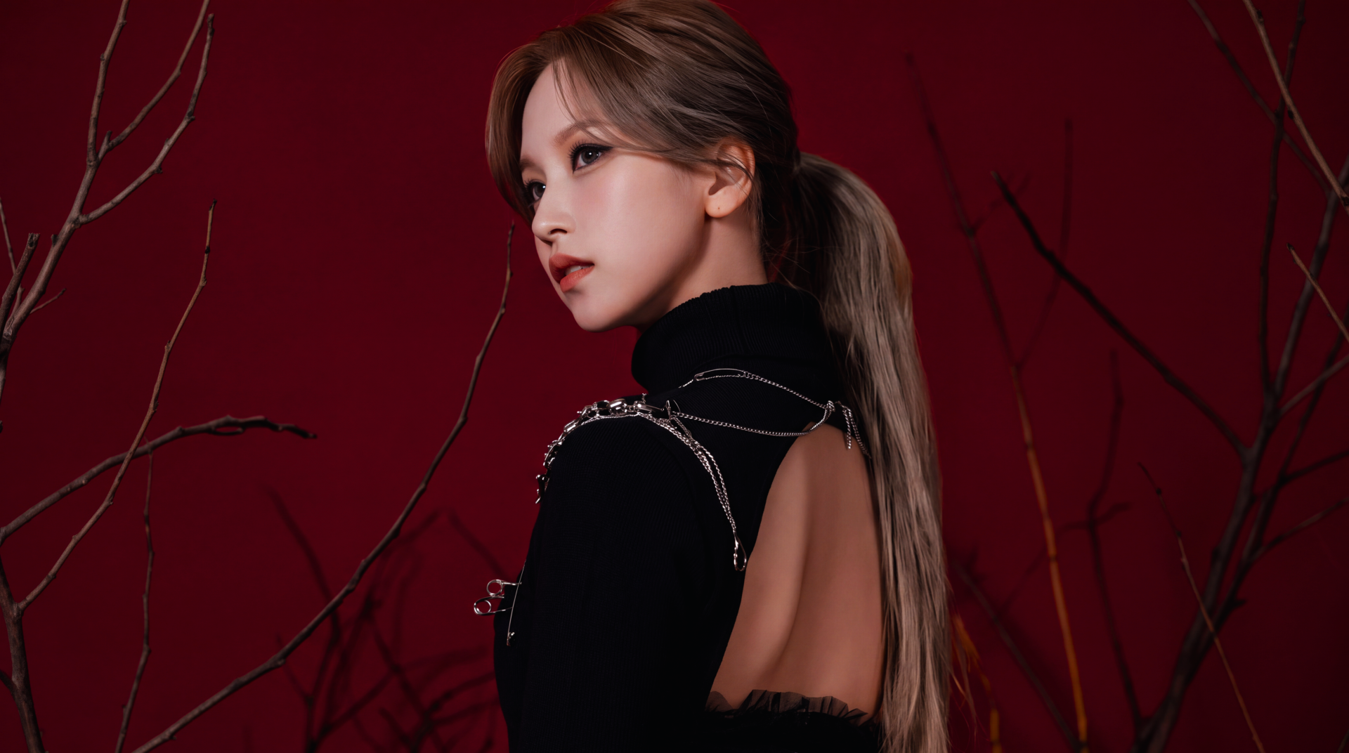 5K desktop wallpaper: side profile of a Japanese model and singer in K-pop–inspired styling, black open-back outfit and ponytail against a deep red background.