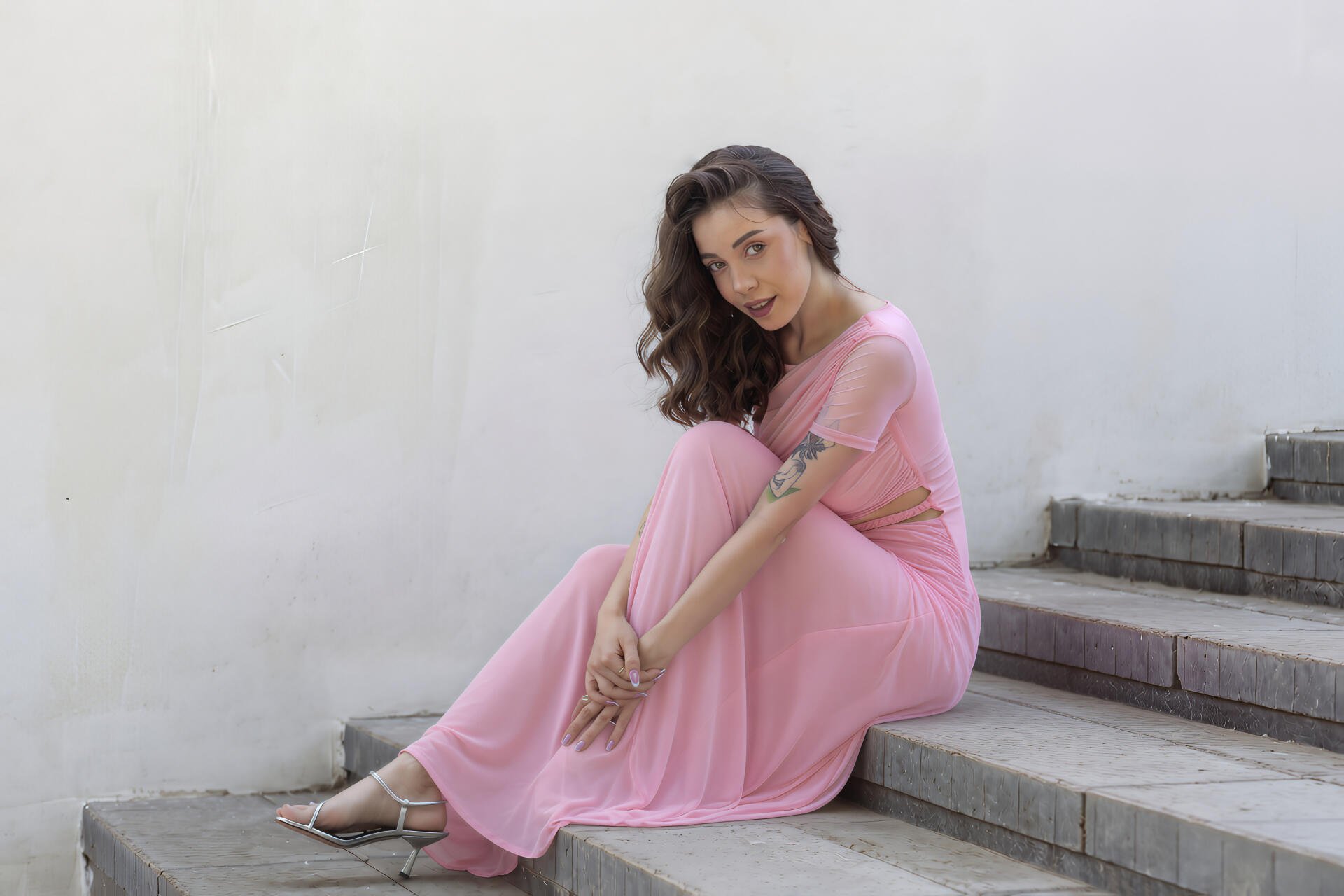 Smiling model girl in a flowing pink dress seated on concrete steps, 4K Ultra HD PC desktop wallpaper background.