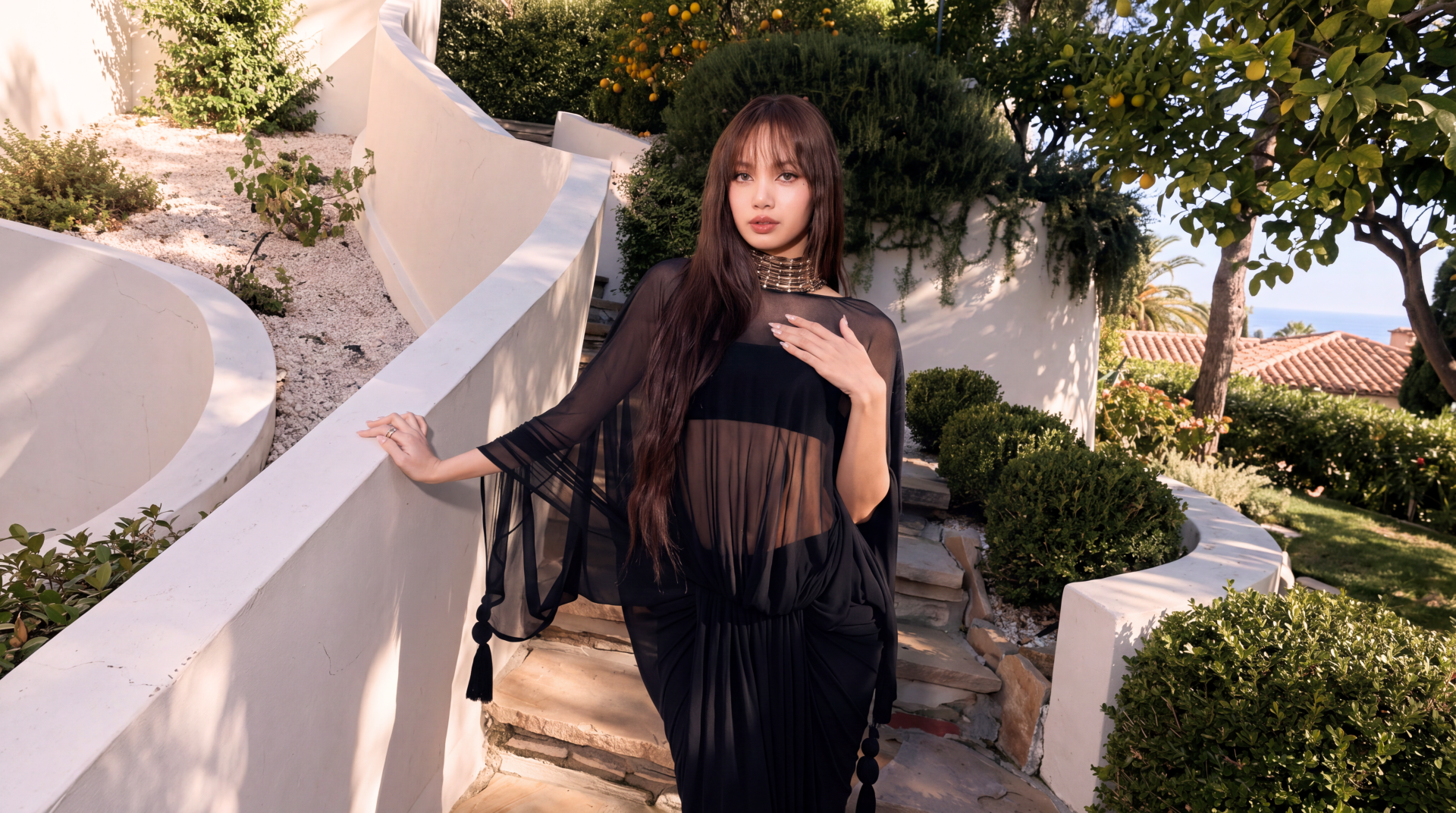 Woman in a sheer black K-pop–inspired outfit posed on a sunlit Mediterranean white-walled terrace with lush greenery — 5K Ultra HD desktop wallpaper.