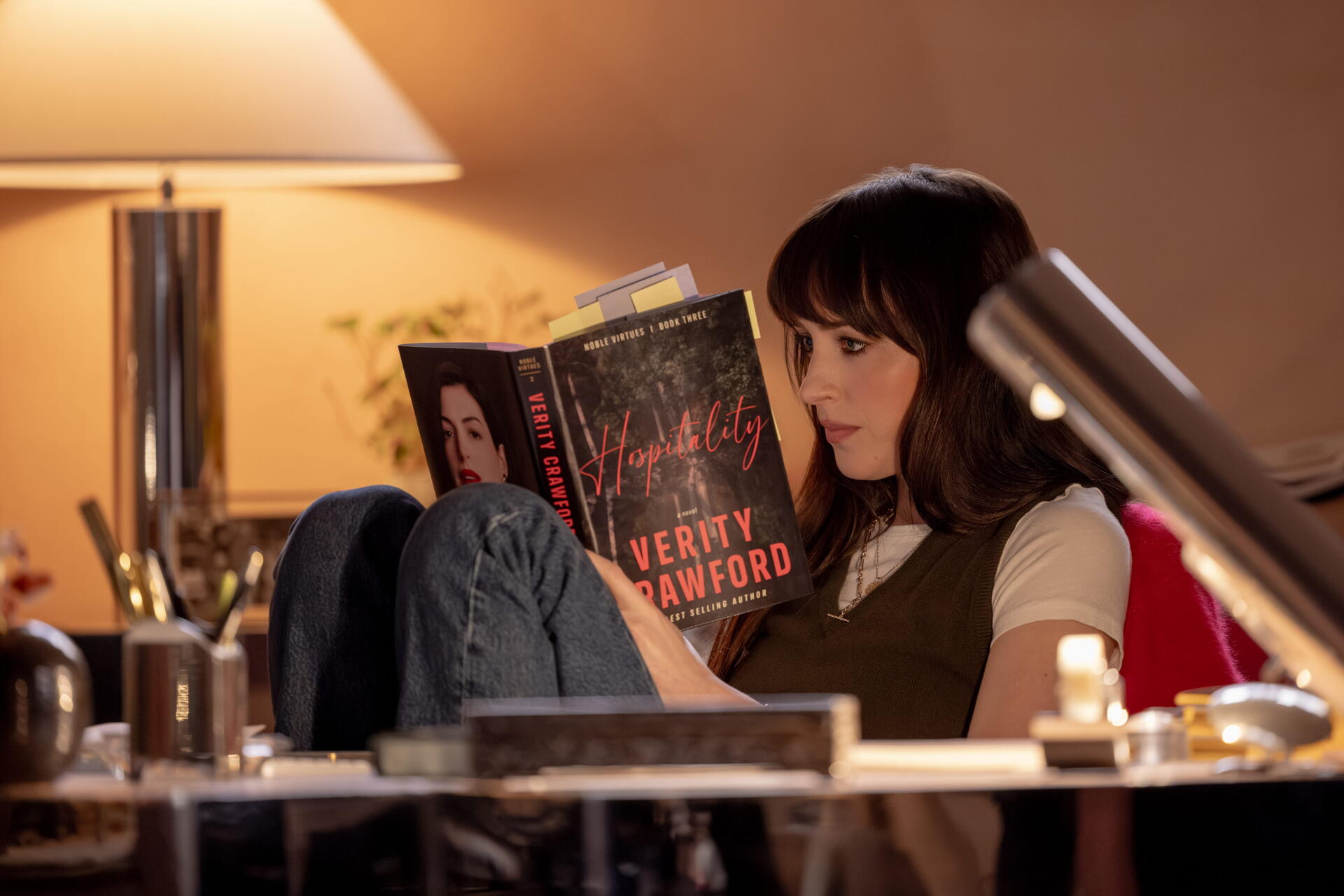 Dakota Johnson reads Verity in a warmly lit room, featured in a 4K Ultra HD PC desktop wallpaper and background for Verity (2026).
