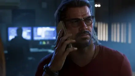 Raul Bautista from Grand Theft Auto VI in a moody 4K Ultra HD PC desktop wallpaper, holding a phone in a dim control-room, video game background.