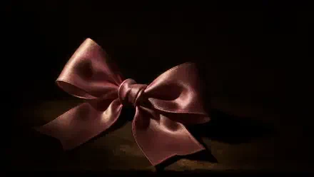 Pink satin bow on a shadowed dark surface, rendered as a 4K Ultra HD PC desktop wallpaper and background.