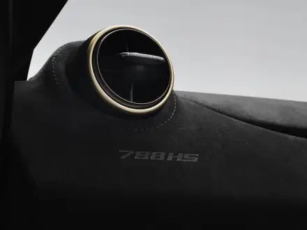 Close-up of a McLaren 788HS dashboard with a round gold-trimmed air vent and embossed 788HS on Alcantara — 8K Ultra HD PC desktop wallpaper/background of a McLaren vehicle.
