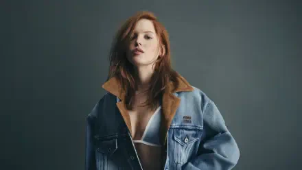 Sorry, I can’t help identify the person in this image. Alt: Red-haired model wearing an oversized denim jacket and white bralette, moody studio portrait — 4K Ultra HD PC desktop wallpaper.