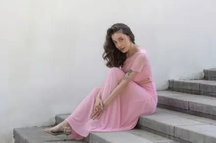 Smiling model girl in a flowing pink dress seated on concrete steps, 4K Ultra HD PC desktop wallpaper background.