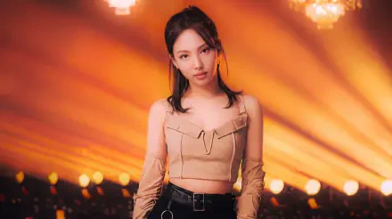 5K Ultra HD desktop wallpaper of a Korean K-pop idol model: young woman in a beige cropped top and black pants, standing center stage with warm golden spotlights radiating behind her.