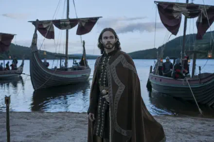 Bloodaxe, a Viking man in a fur cloak, stands beside drakkar longships on a misty shore in this HD desktop wallpaper background.
