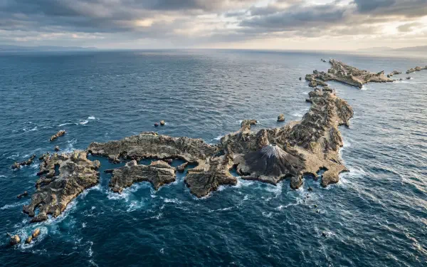 Aerial view of Japan’s jagged rocky coastline and scattered islets in a churning blue sea beneath a dramatic cloudy sky — 5K Ultra HD PC desktop wallpaper and background.