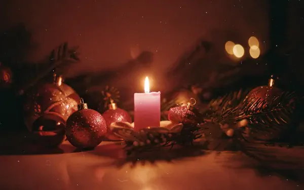 Warm glowing Christmas candle amid evergreen branches and red baubles with soft bokeh — 4K Ultra HD PC desktop wallpaper background.