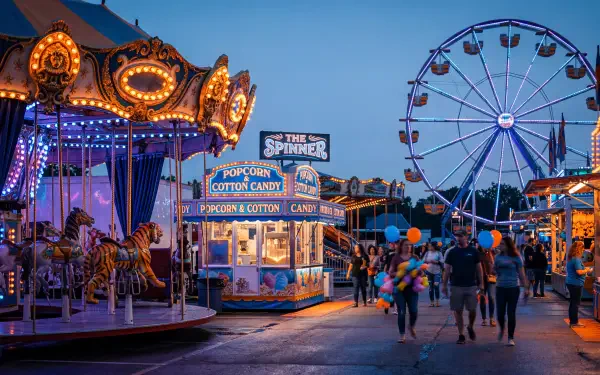 Dusk fair scene: glowing carousel, Ferris wheel, popcorn stand and families walking — 5K Ultra HD PC desktop wallpaper and background.