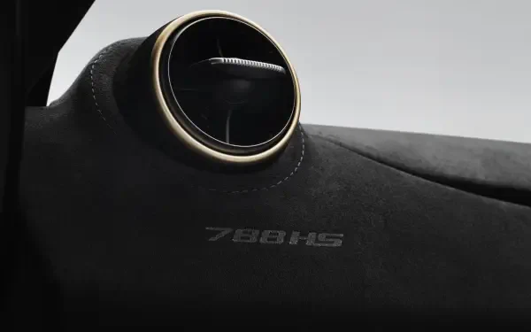 Close-up of a McLaren 788HS dashboard with a round gold-trimmed air vent and embossed 788HS on Alcantara — 8K Ultra HD PC desktop wallpaper/background of a McLaren vehicle.