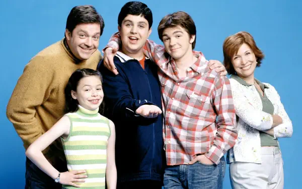 HD PC desktop wallpaper of a smiling sitcom cast — two teen boys, a girl and two adults posed against a blue background.