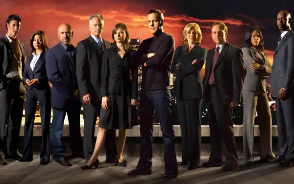 HD PC desktop wallpaper — 24: a group of serious men and women in professional attire stand on a rooftop before a fiery sunset skyline, a central figure posed with arms crossed.