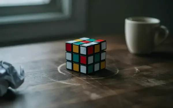 4K Ultra HD PC desktop wallpaper: a Rubik's Cube puzzle cube on a wooden table, soft window light and a coffee mug in the background.