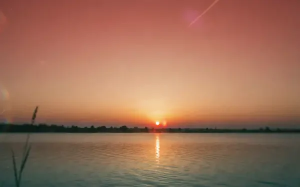 2K Quad HD PC desktop wallpaper and background: summer sunset over calm water, orange-pink sky with the sun low on the horizon and its reflection rippling on the lake.