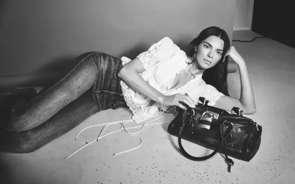 Black-and-white 4K Ultra HD PC desktop wallpaper of a woman reclining on the floor in jeans and a ruffled blouse, propped on one elbow beside a leather handbag.