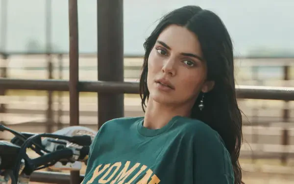 4K Ultra HD desktop wallpaper of a female model in a green tee leaning by a railing outdoors with a motorcycle behind her, soft natural light and a neutral expression.