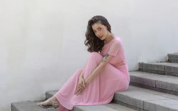 Smiling model girl in a flowing pink dress seated on concrete steps, 4K Ultra HD PC desktop wallpaper background.