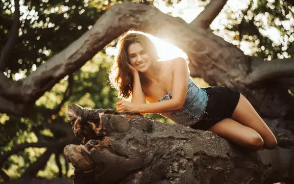 Girl model lying on a gnarled tree branch at sunset, warm golden backlight and bokeh — 5K Ultra HD PC desktop wallpaper/background.