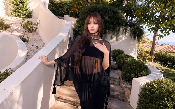 Woman in a sheer black K-pop–inspired outfit posed on a sunlit Mediterranean white-walled terrace with lush greenery — 5K Ultra HD desktop wallpaper.