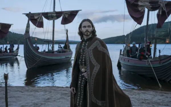Bloodaxe, a Viking man in a fur cloak, stands beside drakkar longships on a misty shore in this HD desktop wallpaper background.