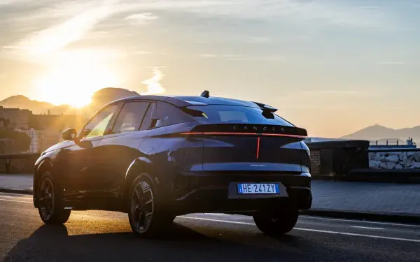 Blue Lancia Gamma electric SUV driving at sunset, featured in an HD PC desktop wallpaper background.