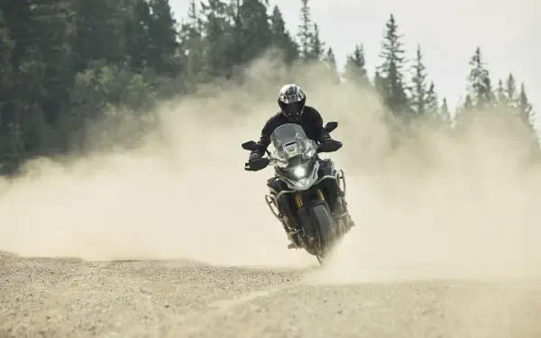 Motorcyclist riding a Triumph Tiger 1200 through a dusty forest trail, captured in an 8K Ultra HD desktop wallpaper.