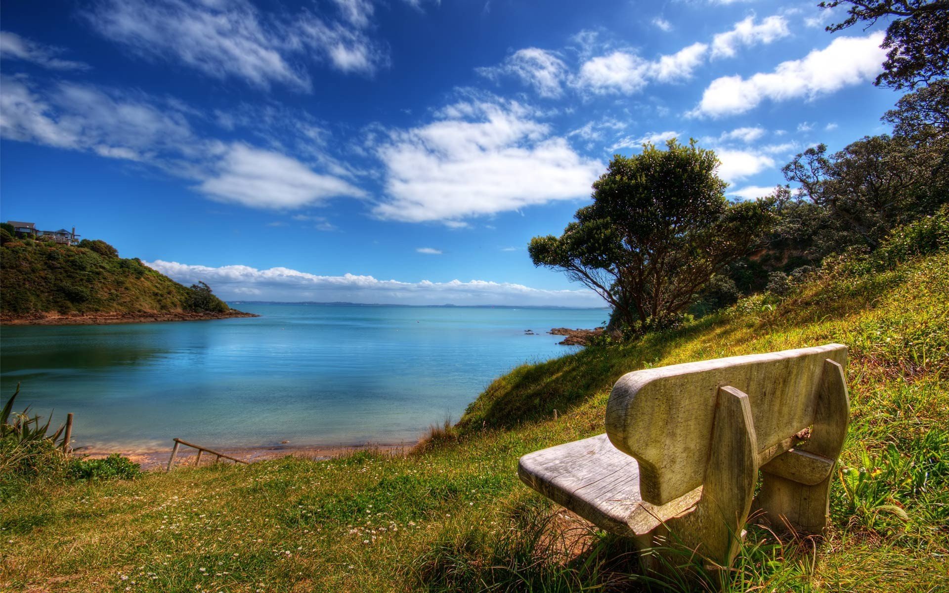 HD PC desktop wallpaper: man-made stone bench on a grassy bluff overlooking a tranquil bay with blue sky and scattered clouds.