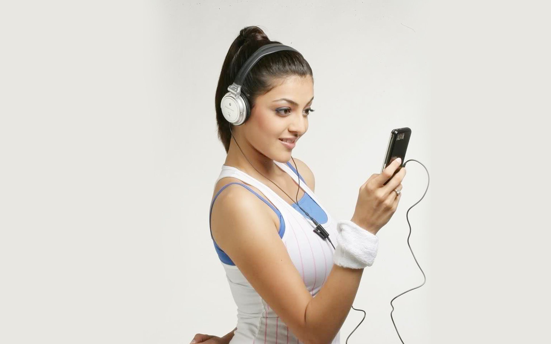 Kajal Aggarwal enjoying music while wearing headphones, showcasing a vibrant and energetic look. This HD wallpaper captures her playful spirit and style.