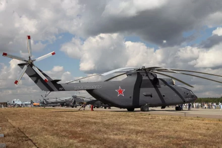 4K Ultra HD PC desktop wallpaper: a gray Mil Mi-26 military helicopter parked on a grassy field under dramatic clouds, red star insignia visible, airshow crowd in the distance.