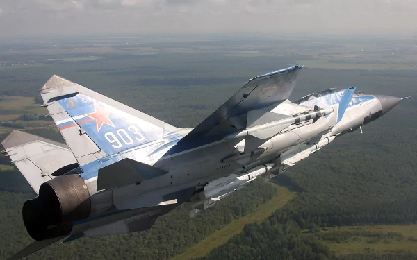 Mikoyan MiG-31 jet fighter in flight over a forested landscape, military aircraft imagery rendered as a 2K Quad HD PC desktop wallpaper and background, tail number 903 visible.