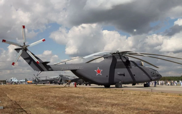 4K Ultra HD PC desktop wallpaper: a gray Mil Mi-26 military helicopter parked on a grassy field under dramatic clouds, red star insignia visible, airshow crowd in the distance.