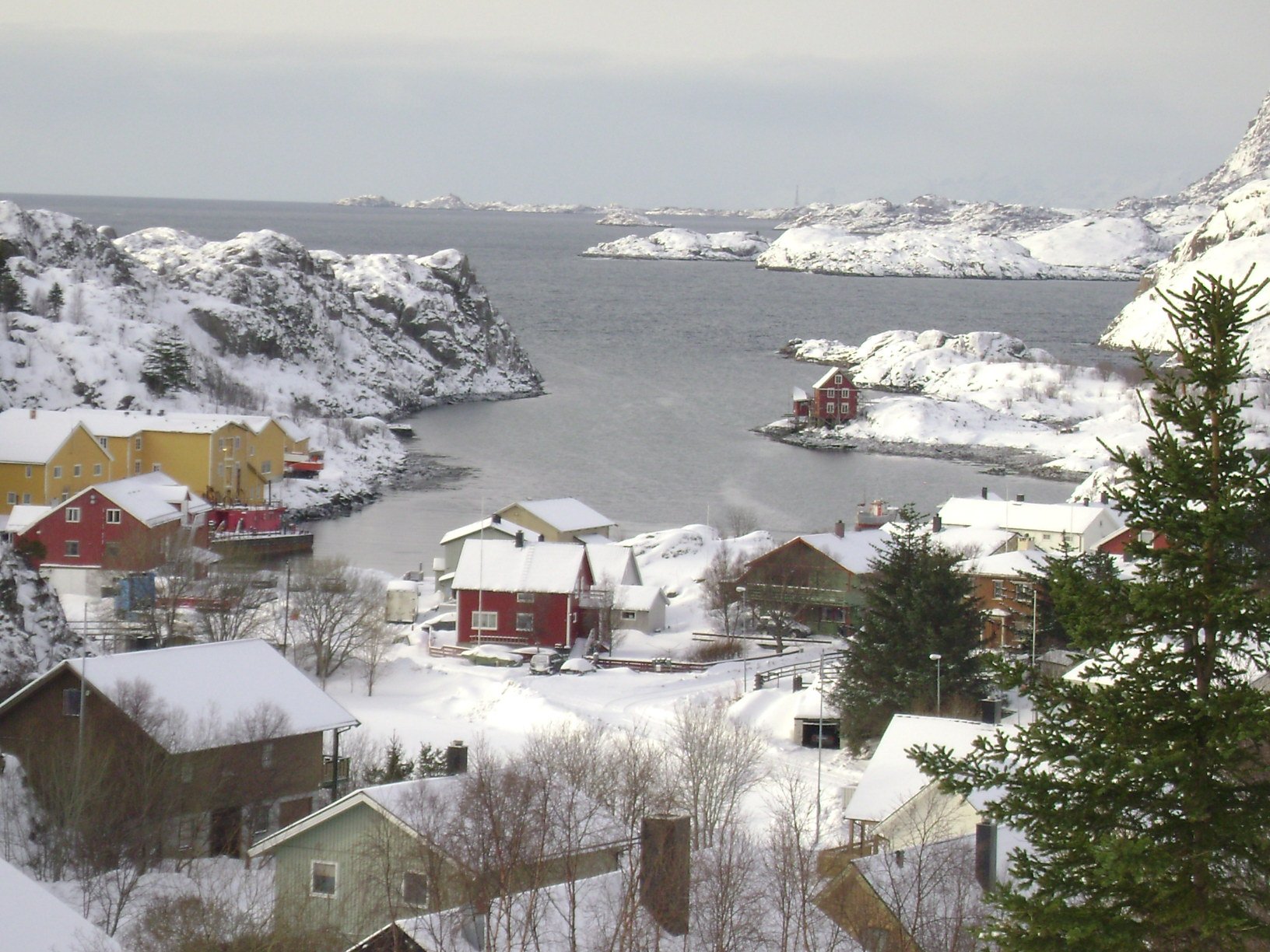 HD desktop wallpaper showcasing a snowy man-made coastal town nestled between rocky cliffs and a calm sea under a cloudy sky.