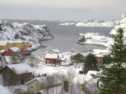 HD desktop wallpaper showcasing a snowy man-made coastal town nestled between rocky cliffs and a calm sea under a cloudy sky.