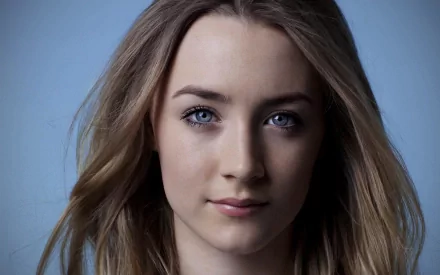 Close-up of actress Saoirse Ronan, featuring her striking blue eyes and softly flowing hair against a smooth blue background. A vibrant HD wallpaper choice for fans.