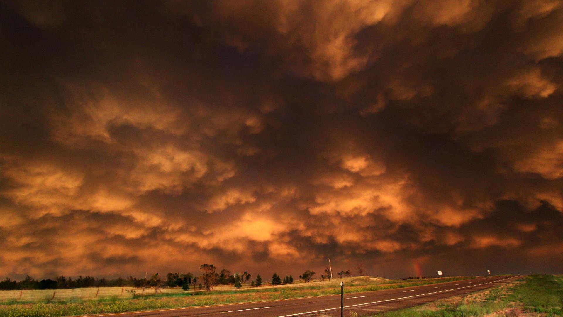 HD PC desktop wallpaper and background: nature cloud scene of dramatic glowing orange storm clouds rolling over a rural road and green fields at dusk.