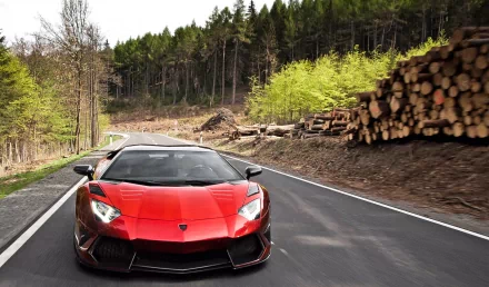 A stunning Lamborghini Aventador drives along a winding road, surrounded by lush green trees and stacked logs, creating a dynamic and vibrant HD desktop wallpaper.