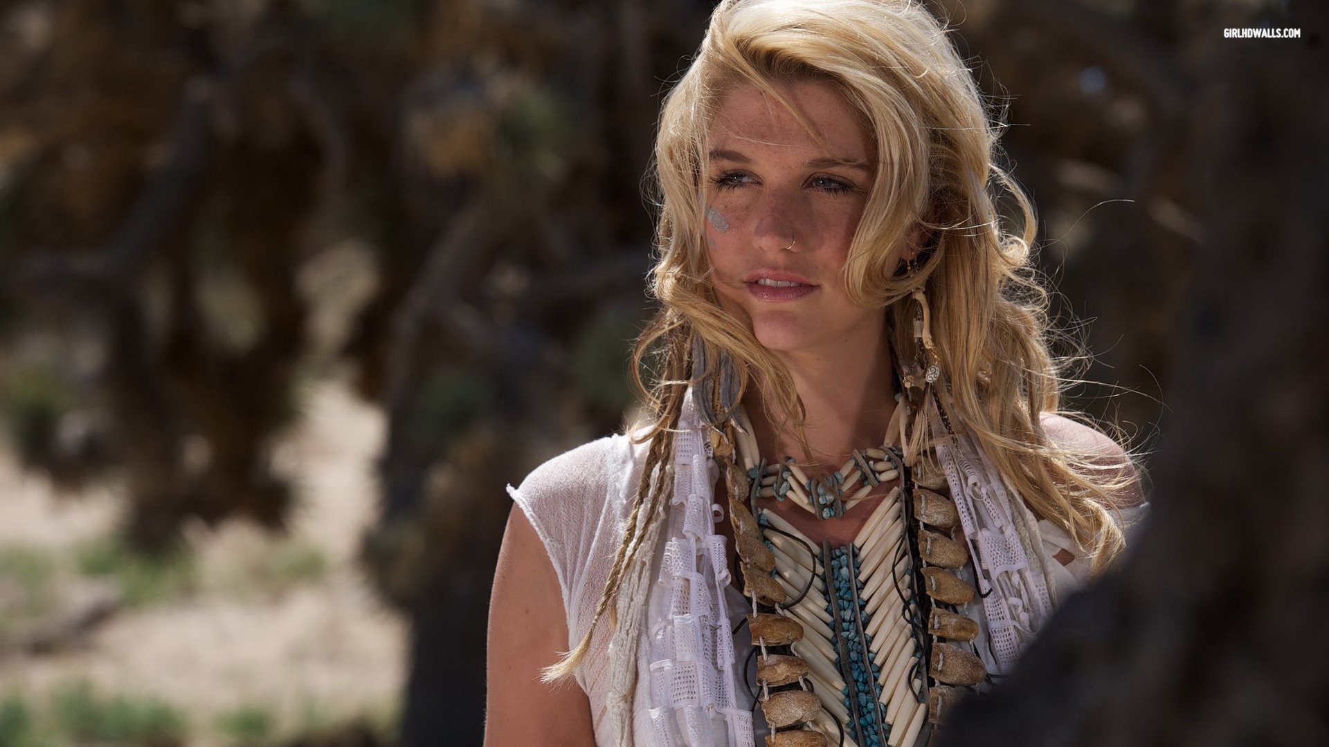 HD PC desktop wallpaper showing a music artist outdoors — sunlit, wind‑blown hair, layered necklaces and bohemian clothing, gazing off camera.