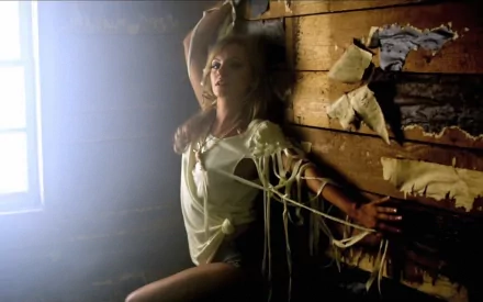 HD desktop wallpaper of music artist Alexandra Stan, posing against a wooden wall in a rustic setting, bathed in soft, natural light from a nearby window.