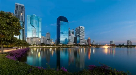 HD desktop wallpaper of Bangkok's city skyline with skyscrapers reflecting on a lake in Thailand during twilight.