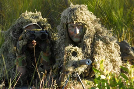 Two military snipers in full camouflage gear conduct an ambush, blending seamlessly into the tall grass environment. HD PC desktop wallpaper and background.
