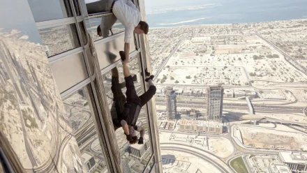 HD wallpaper featuring Tom Cruise as Ethan Hunt in Mission: Impossible - Ghost Protocol, performing a daring stunt on the side of a skyscraper with a cityscape in the background.