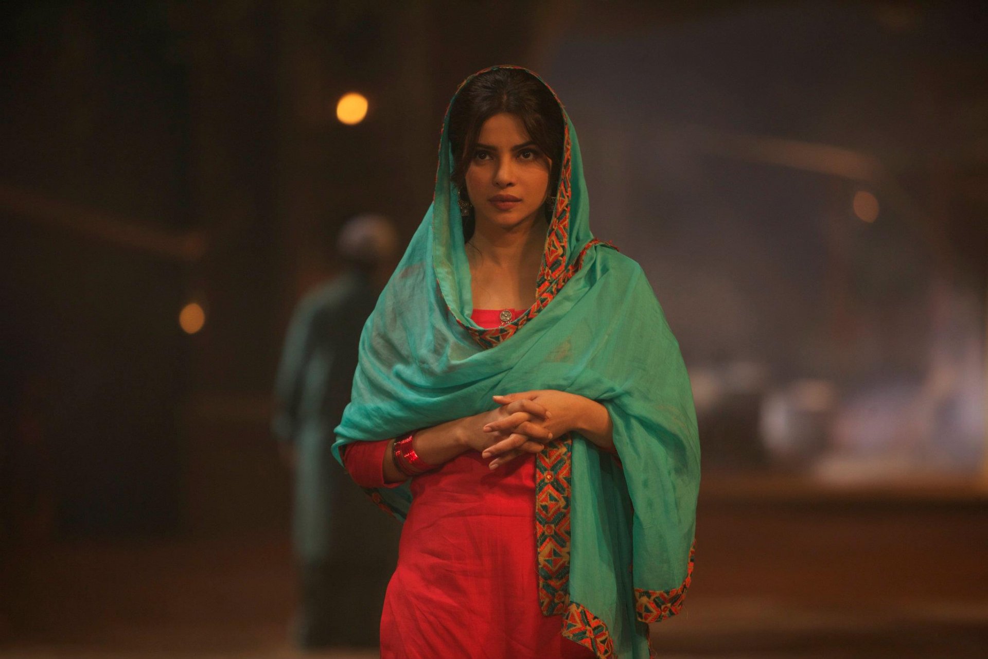 HD PC desktop wallpaper featuring celebrity Priyanka Chopra wearing a red outfit and teal shawl, captured in a softly lit, nighttime street setting.