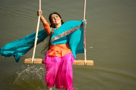 HD desktop wallpaper of celebrity Priyanka Chopra joyfully swinging over water, dressed in vibrant traditional attire with flowing turquoise scarf.