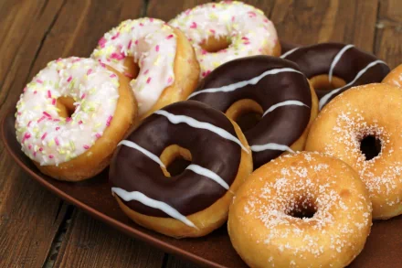 A delicious assortment of doughnuts in various flavors, including chocolate and sprinkles, displayed on a wooden plate, serving as a vibrant 4K Ultra HD desktop wallpaper.