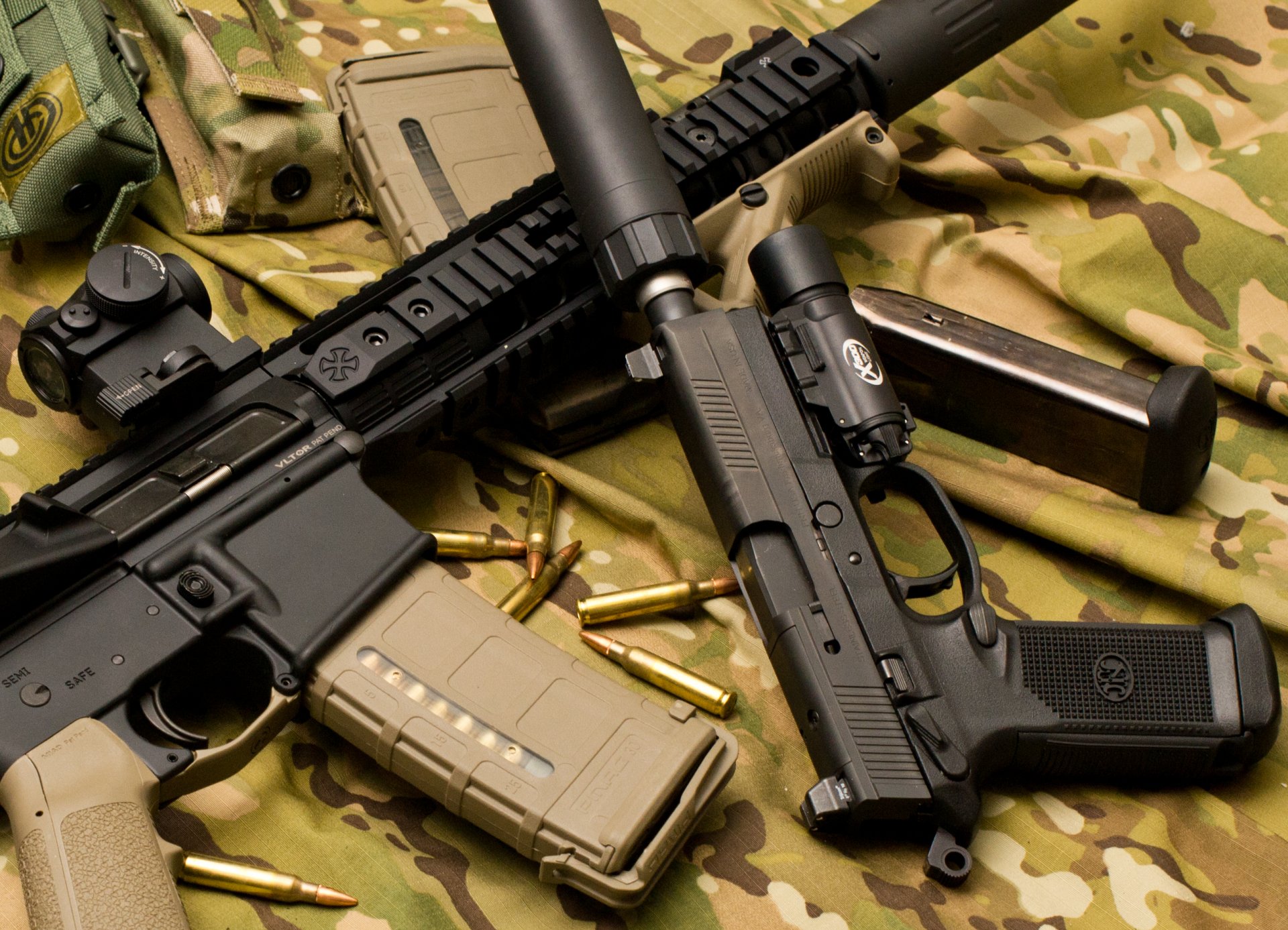 2K Quad HD PC desktop wallpaper showing man-made weapons: an assault rifle and handgun with magazines and loose brass laid out on camouflage fabric.