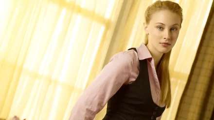 HD PC desktop wallpaper featuring celebrity Sarah Gadon in a soft-lit setting, wearing a light pink shirt with a black vest, against a warm, yellow curtain background.