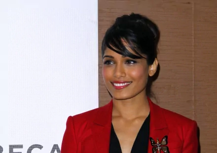 HD wallpaper featuring Freida Pinto in a vibrant red blazer, smiling warmly against a neutral background. A striking celebrity image for desktop display.