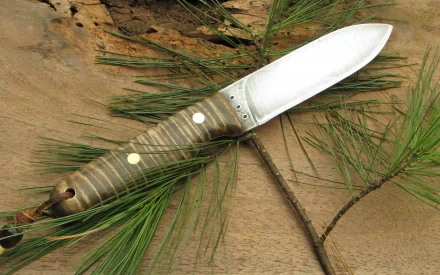 A beautifully crafted knife rests on a wooden surface, surrounded by pine branches, making this HD wallpaper an exceptional choice for desktop backgrounds.